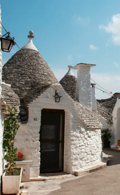 Traditionelle Trulli-Häuser mit kegelförmigen Dächern in einem engen, sonnigen Gassenbereich in Apulien, Italien.