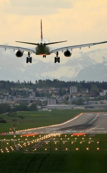 Flugzeug im Landeanflug über Stadt und Landebahn mit Bergen im Hintergrund.