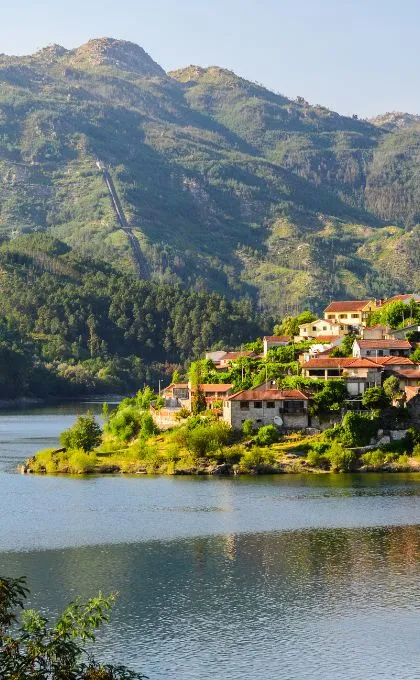 Kleines Dorf mit roten Dächern in den waldreichen Bergen Portugals, gelegen direkt neben einem See.
