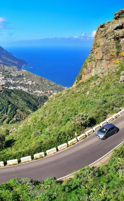 Auto fährt auf einer Straße durch die Berge Spaniens, das Meer im Hintergrund.