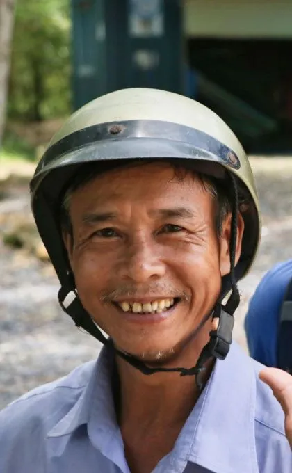 Vietnamese mit einem Rollerhelm auf lächelt in die Kamera.