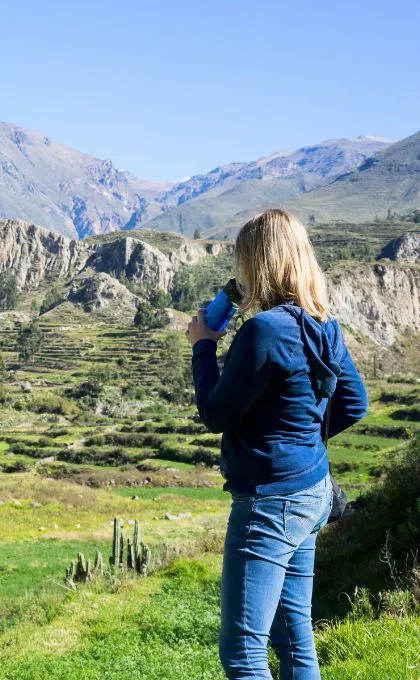 Frau steht vor einer bergigen Landschaft und trinkt aus ihrer Filterflasche.