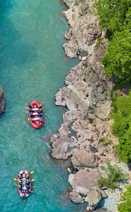 Zwei rote Rafting Boote fahren über einen türkisen Fluss an schroffen Felsen entlang, Albanien.