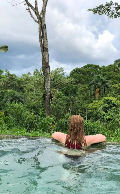 Frau lehnt sich an den Rand eines Infinity Pools und schaut auf den Regenwald, der sie unmittelbar umgibt.