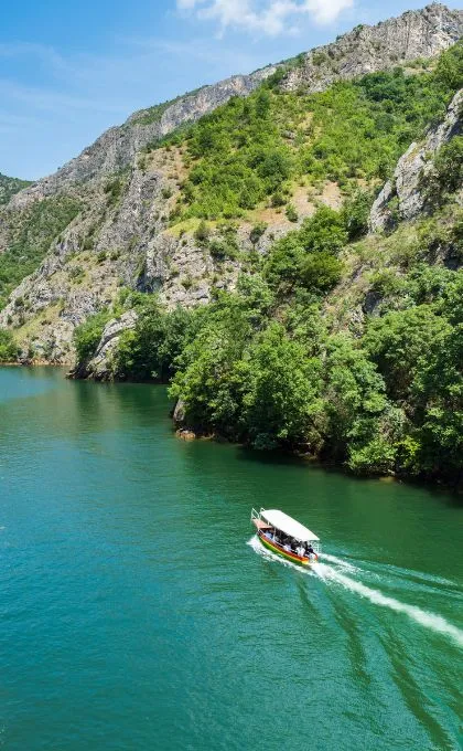 Überdachtes Boot fährt über das türkise Wasser einer von Felsen umgebenen Schlucht in Mazedonien.