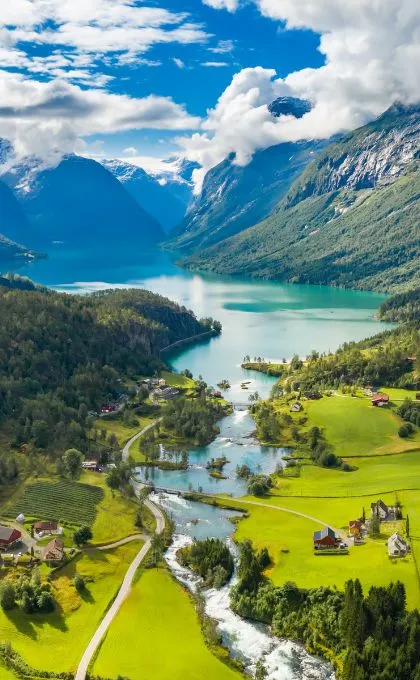 Norwegische Landschaft mit einem türkisen Fjord, steilen Hängen und Wiesen mit einigen Häusern am Wasser.