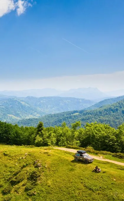 Zwei Reisende sitzen vor Ihren Jeep auf einer Wiese mitten in den Bergen Montenegros.