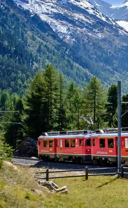 Roter Zug fährt vorbei an einer beeindruckenden Berglandschaft.