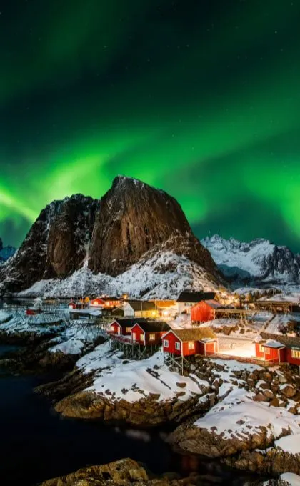 Die Nordlichter in Norwegen scheinen am Himmel über einem schneebedeckten Dorf in den Bergen.