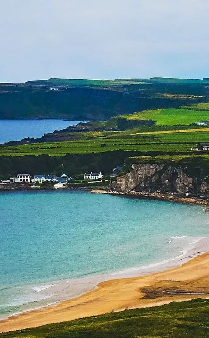 Blaues Küstenwasser trifft auf steile Klippen mit grünen Wiesen darüber, beim Wild Atlantic Highway in Irland.