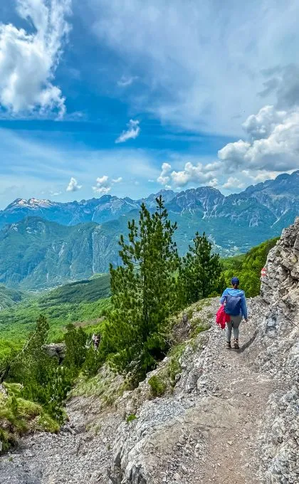 Frau läuft über einen schmalen Wanderweg in Albanien neben den Felsen mit einer tollen Aussicht auf die Berge.