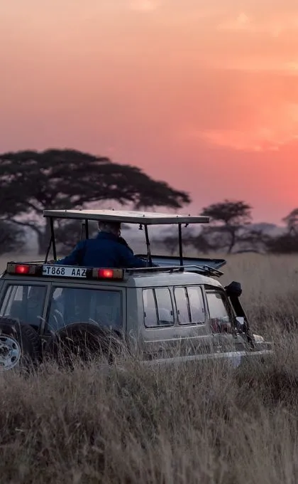 Safari-Jeep steht bei Sonnenaufgang in der Savanne Tansanias.