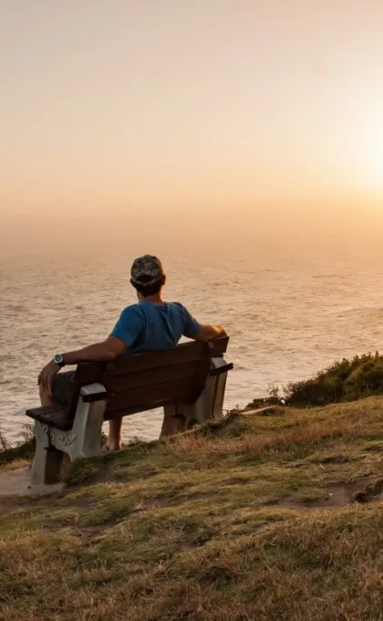 Ein Mann sitzt auf einer Bank an der Küste und genießt die Aussicht auf den Sonnenuntergang über dem Ozean.