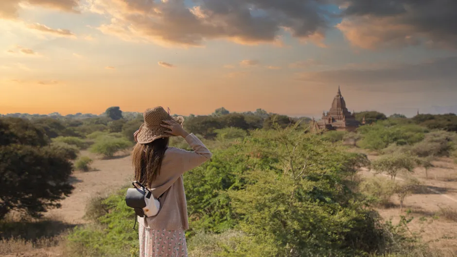 Eine Frau steht während ihrer Rundreise in Myanmar in der Landschaft und trägt einen Rucksack