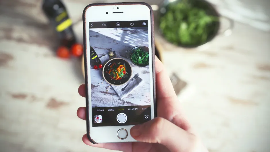 Eine Hand hält ein Smartphone auf dem ein Bild vom Kochkurs von der virtuellen Tour abgebildet ist