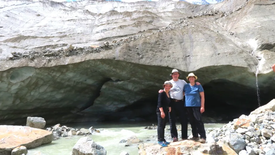 Reisende stehen vor einer Höhle in Georgien, daneben fließt ein Wasserfall.