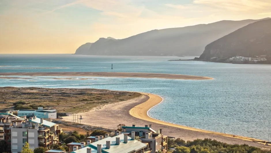 Im Vordergrund ist ein Strand zu sehen und im Hintergrund Berge im Morgengrauen.