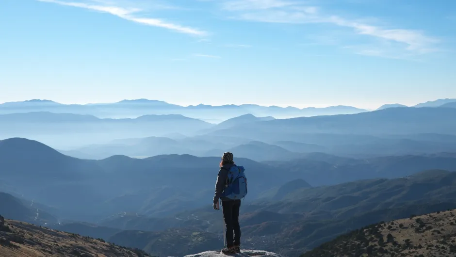 eine Person, die auf einem felsigen Vorsprung steht und eine weite Landschaft aus Bergen und Tälern überblickt.