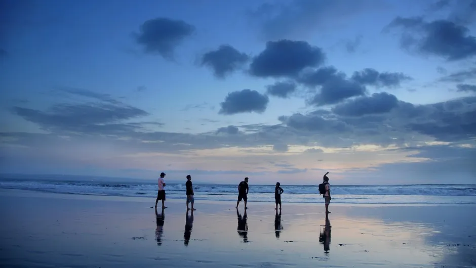 Eien Gruppe von Jungs steht auf dem Strand beim Sonnenuntergang.