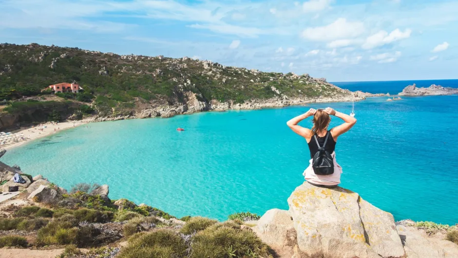 Ein Person, die auf einem Felsen sitzt und auf eine wunderschöne Küstenlandschaft blickt.