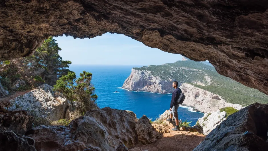 individualreise Sardinien: Person am Höhleneingang mit Blick aufs Meer und Klippen.