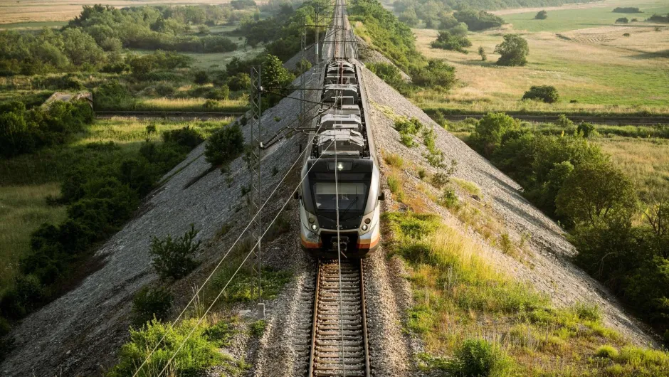 Zug durchquert grüne Landschaft auf einem Damm – unterwegs Richtung Montenegro.