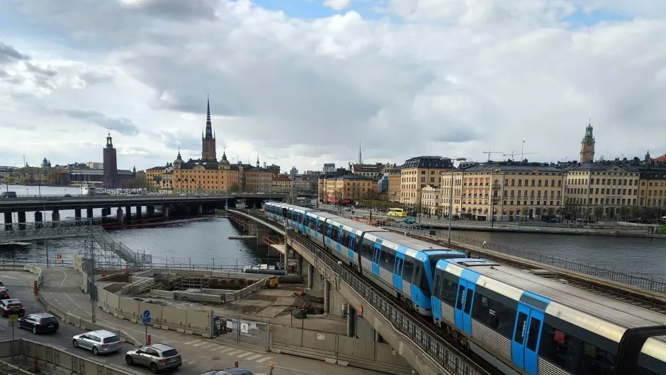 Ein Blauer Zug fährt über eine Brücke in Stockholm mit Blick auf die Altstadt und das Stadshuset am Wasser.