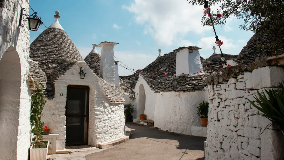 Traditionelle Trulli-Häuser mit kegelförmigen Dächern in einem engen, sonnigen Gassenbereich in Apulien, Italien.