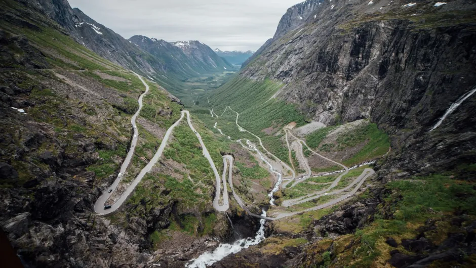 Serpentinenstraße schlängelt sich durch ein steiles Gebirgstal mit Wasserfällen und grünen Hängen, aus der Vogelperspektive aufgenommen.