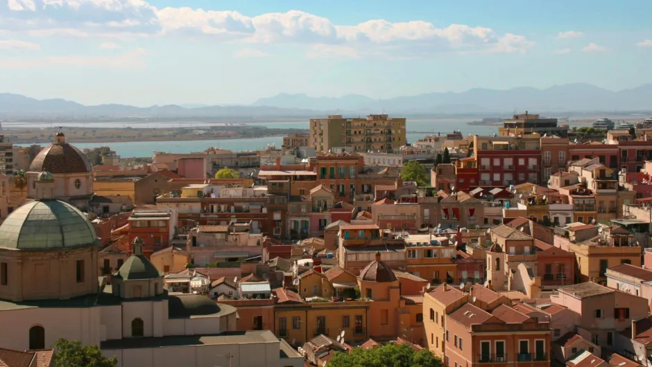 Panoramablick über die Dächer von Cagliar mit Kirche im Vordergrund, dem Meer und Bergen im Hintergrund.