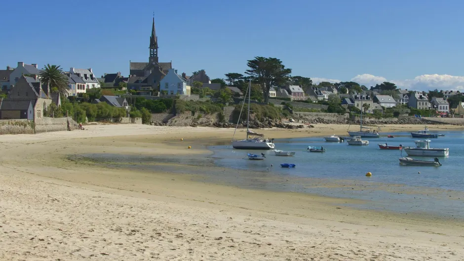 Sandstrand mit kleinen Booten vor einem Dorf mit Kirche und typischen Steinhäusern an der Küste.