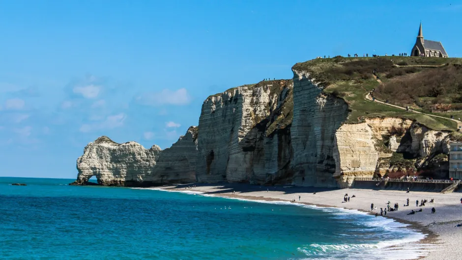 Kreidefelsen und Felsbogen bei Étretat in der Normandie mit Strand, türkisblauem Meer und kleiner Kapelle auf den Klippen.