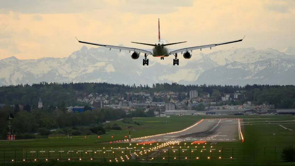 Flugzeug im Landeanflug über Stadt und Landebahn mit Bergen im Hintergrund.