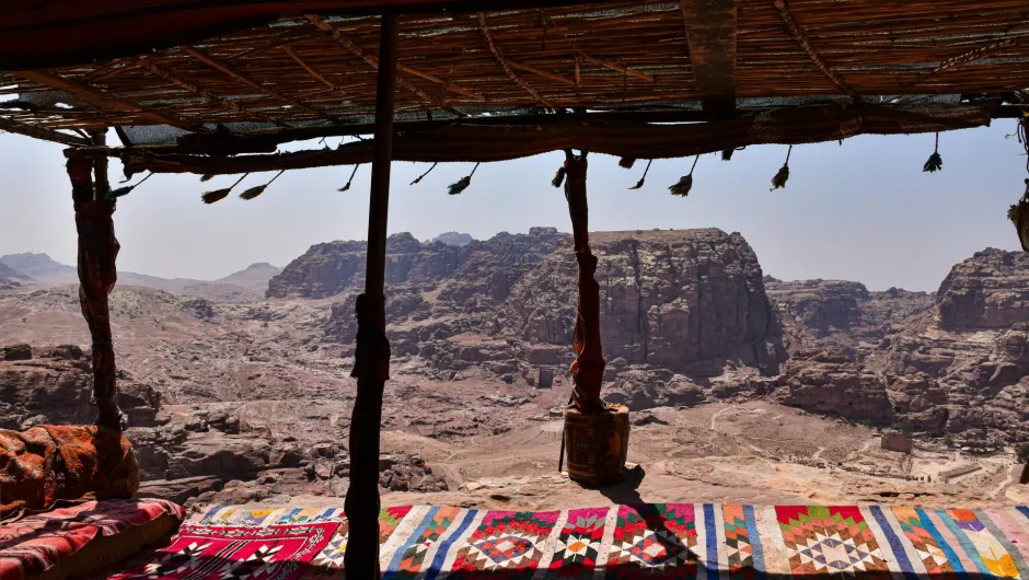 Blick von einem schattigen Beduinenzelt mit bunten Teppichen auf die Felsenlandschaft von Petra in Jordanien.