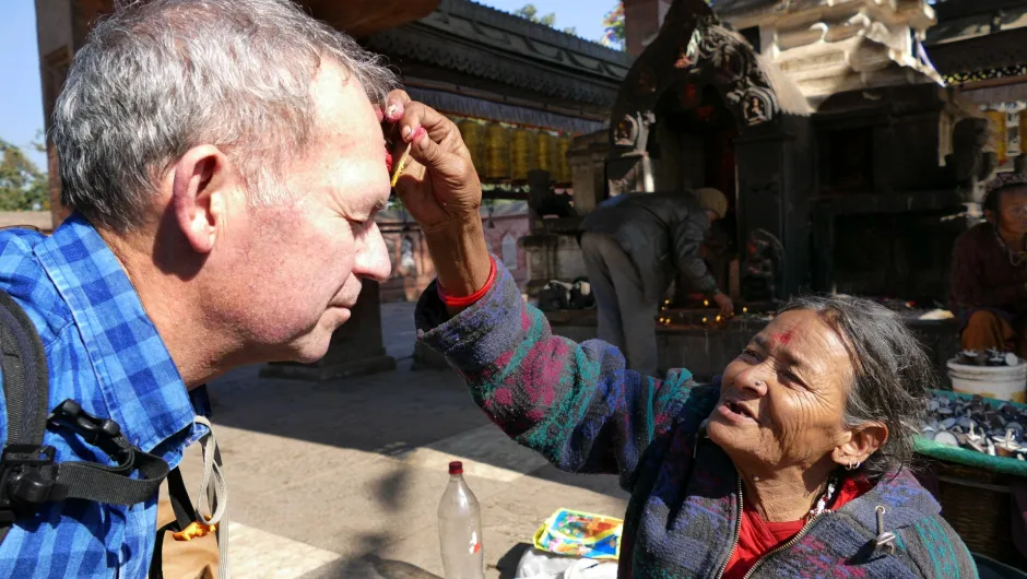 Lokale Frau gibt einem Reisenden in einer Tempelanlage in Kathmandu eine rote Tika auf die Stirn.
