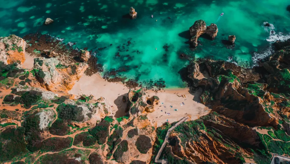 Luftaufnahme einer felsigen Küste mit türkisfarbenem Wasser, Sandstrand und Felsformationen im Meer.
