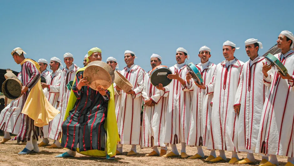 Traditionelle Musiker in Marokko stehen in weißen Gewändern mit Trommeln und Tamburinen unter blauem Himmel.