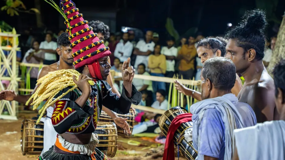 Traditioneller Tänzer in Sri Lanka mit auffälligem Kopfschmuck tritt bei einer abendlichen Zeremonie vor Musikern und Publikum auf.