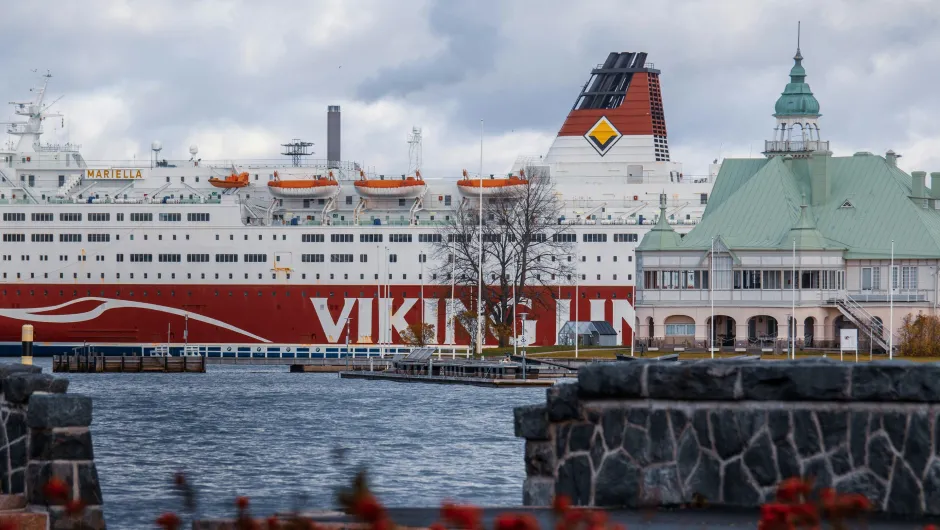 Viking-Line-Fähre Mariella im Hafen von Helsinki vor einem historischen Gebäude mit grünem Kupferdach, bewölkter Himmel über der Ostsee.