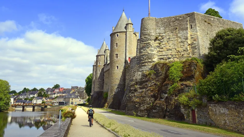 Radfahrer auf einem Weg entlang des Flusses Oust vor dem imposanten Château de Josselin in der Bretagne.