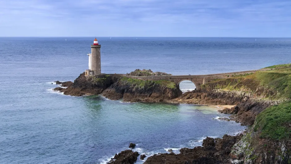 Leuchtturm von Kermorvan an der felsigen Küste der West-Bretagne mit Steinbrücke und Atlantik im Hintergrund.