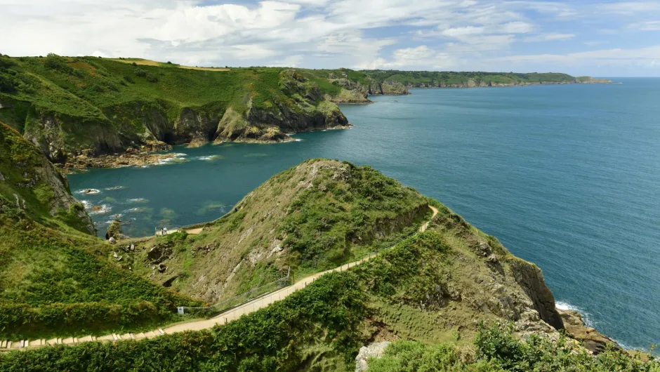 Grüne Steilküste der Kanalinseln mit Wanderweg entlang der Felsen und Blick auf das blaue Meer.