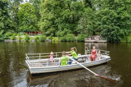 Kinder und Eine Frau sitzen in einem RUderboot über den Fluss.