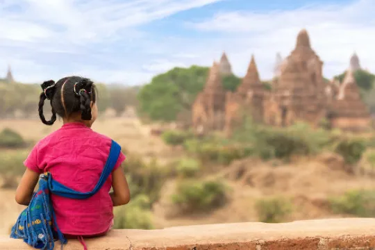Ein Kind sitzt während der Myanmar mit Kindern Reise auf einer Mauer