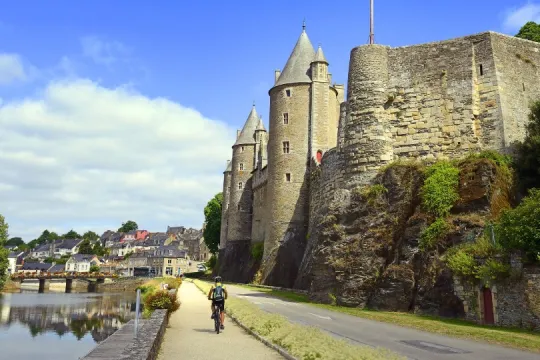 Radfahrer auf einem Weg entlang des Flusses Oust vor dem imposanten Château de Josselin in der Bretagne.